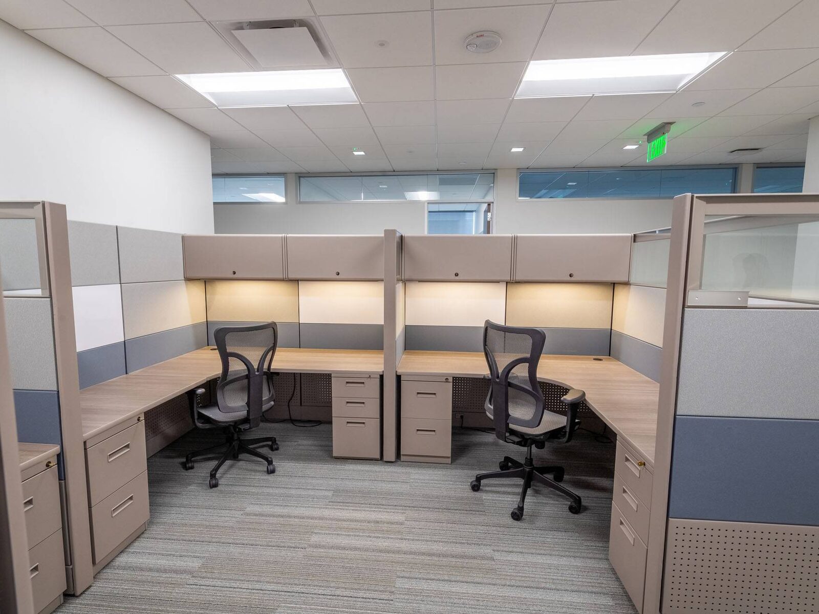 Two cubicle workstations with task lighting and overhead storage in a compact office